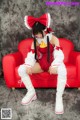A woman in a red and white outfit sitting on a red couch.