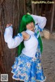A woman with green hair leaning against a tree.