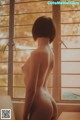 A nude woman standing in front of a window.