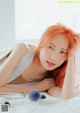 A woman with bright orange hair laying on a bed.